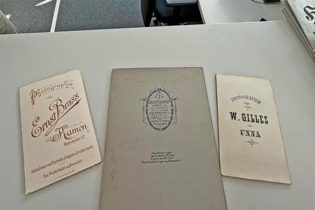 Karten mit den Emblemen der frühen Fotografen Ernst Brass aus Kamen sowie Julius Flechtner und W. Gilles aus Unna liegen auf einem Tisch. Karten mit den Emblemen der frühen Fotografen Ernst Brass aus Kamen sowie Julius Flechtner und W. Gilles aus Unna liegen auf einem Tisch.
