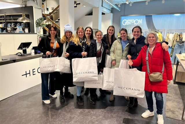 Neun Frauen stehen mit Einkaufstüten im Modehaus Heckmann.