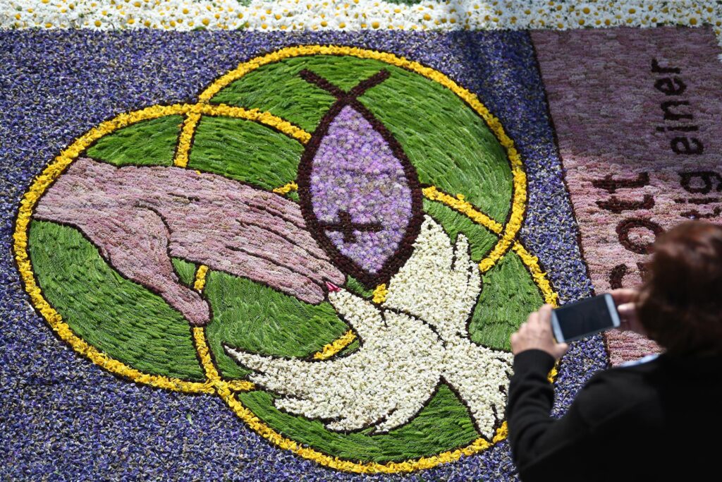 Eine Frau fotografiert an Fronleichnam während der Prozession Kirchenmotive in einem Blumenteppich. Eine Frau fotografiert an Fronleichnam während der Prozession Kirchenmotive in einem Blumenteppich.