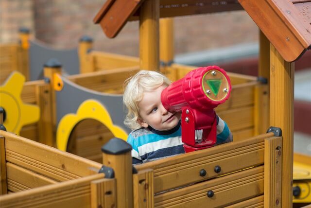 EIn Kleindkind spielt auf einem Spielplatz und schaut durch ein Fernrohr.