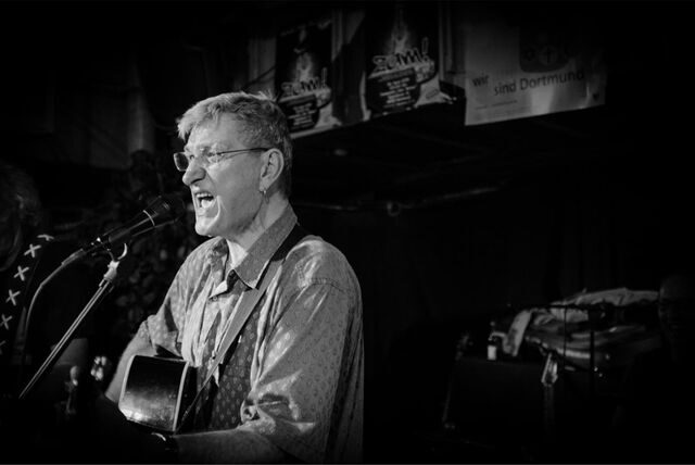 Zu sehen ist Johannes Diehl, der Gitarre spielt und singt.