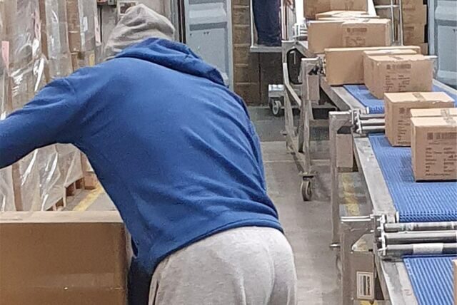 Ein Arbeiter packt in den Metro-Hallen in Marl Kartons auf ein Band.