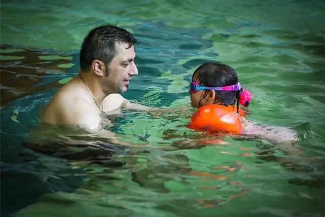 Ein Vater übt mit seiner Tochter in einem Wasserbecken Schwimmen.