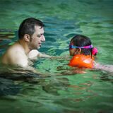 Ein Vater übt mit seiner Tochter in einem Wasserbecken Schwimmen.