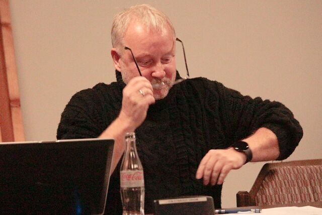 Dietmar De Sacco zieht seine Brille an. Vor ihm steht eine halbvolle Glasflasche Coca Cola light und ein aufgeklappter Laptop