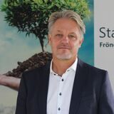 Alexander Loipfinger, Geschäftsführer von den Stadtwerken Fröndenberg Wickede, steht vor einem Plakat, dass eine Weltkugel zeigt und einen Baum mit Wurzeln, die jeweils von einer Hand getragen werden.
