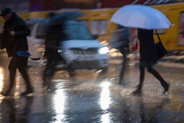 Passanten mit Regenschirmen gehen während eines Gewitters über die Straße.
