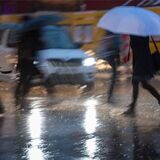 Passanten mit Regenschirmen gehen während eines Gewitters über die Straße.