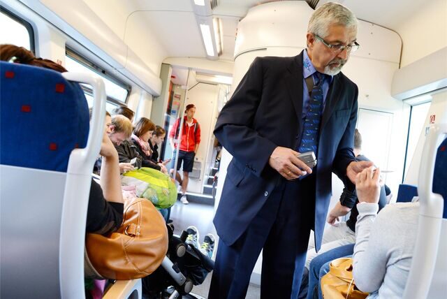 Ein Fahrkartenkontrolleur steht in einer Bahn und kontrolliert Fahrscheine.