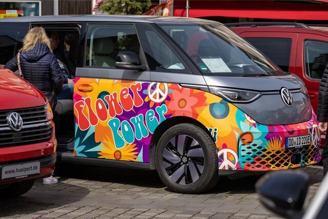 Die Karosserie eines elektrisch betriebenen VW-Busses ist mit bunten Blumen und dem Schriftzug „Flower Power“ gestaltet.