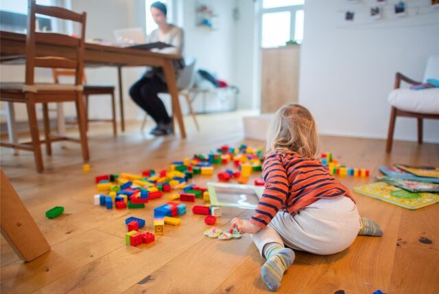 Ein zweijähriges Kind spielt im Wohnzimmer, während seine Mutter Zuhause im Homeoffice an einem Laptop arbeitet. Der Rückzug vom Arbeitsplatz ins Homeoffice soll ein zentraler Baustein im Kampf gegen die Corona-Pandemie werden.