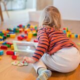 Ein zweijähriges Kind spielt im Wohnzimmer, während seine Mutter Zuhause im Homeoffice an einem Laptop arbeitet. Der Rückzug vom Arbeitsplatz ins Homeoffice soll ein zentraler Baustein im Kampf gegen die Corona-Pandemie werden.