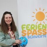 Zu sehen sind zwei junge Frauen vor einem Plakat mit der Aufschrift „Ferienspaß in Schwerte“.