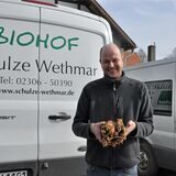 Ein Mann steht vor einem Wagen und hält Rüben in der Hand.
