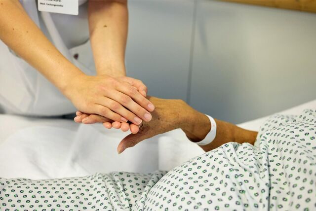 Eine Medizinische Fachangestellte hält die Hand einer Patientin.