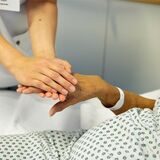 Eine Medizinische Fachangestellte hält die Hand einer Patientin.
