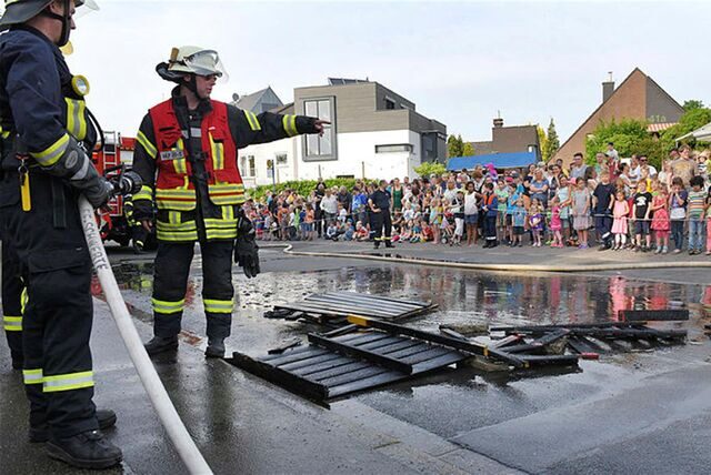 Zu sehen sind Feuerwehrmänner bei einer Schauübung. Viele Kinder und Erwachsene schauen zu.