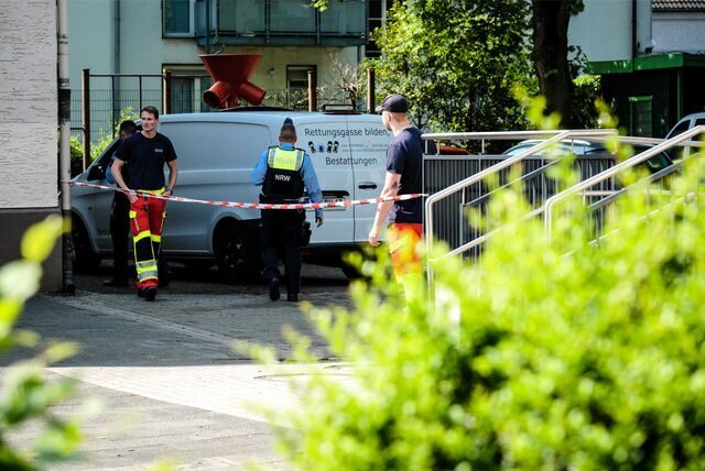 Ein Leichenwagen steht auf einem Schulhof, davor Flatterband sowie Einsatzkräfte von Polizei und Feuerwehr.