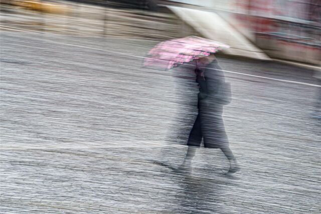 Eine Frau eilt bei Regenwetter mit einem Regenschirm in der Innenstadt.