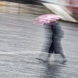 Eine Frau eilt bei Regenwetter mit einem Regenschirm in der Innenstadt.