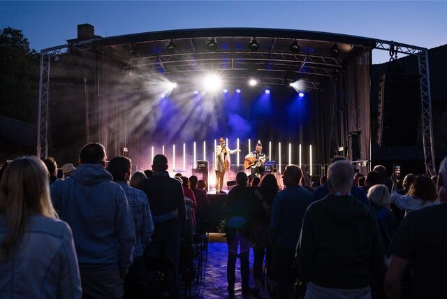 Für die Sommerbühne 2025 auf Haus Opherdicke ist der Vorverkauf gestartet. Auf dem Bild stehen mehrere Zuschauer vor der Bühne und hören den Musikern zu. (Archiv)