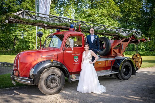 Das Brautpaar Maren und Miro Volkmer steht an einem historischen Einsatzfahrzeug der Feuerwehr Herten.