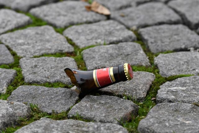 Der Flaschenhals einer Bierflasche liegt auf Pflastersteinen.