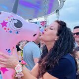 Eine Frau posiert mit einem aufblasbaren Einhorn vor der Festivalbühne beim Sunset Beach Festival.
