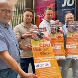 Rolf Weißner und Martin Cyperski von der CDU (v. l.) präsentieren zusammen mit den Gastronomen Markus Bickmann und Andreas Nozar das Plakat fürs CDU-Weinfest am 8. Juli 2023.