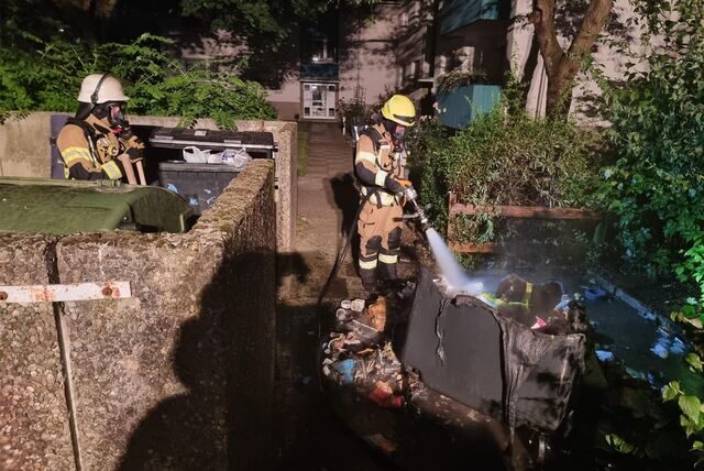Ein Feuerwehrmann löscht eine brennende Mülltonne.