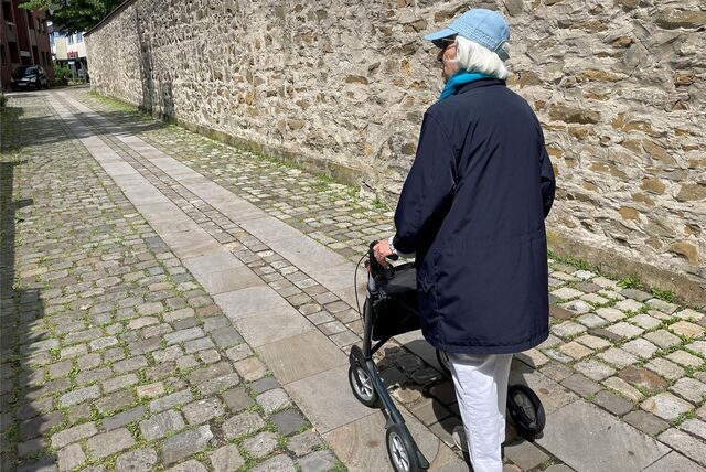 Irmgard Rüsing demonstriert, wie sie mit dem Rollator durch die kleine Gasse am Kloster geht. Dabei bleibt sie schon mal an den defekten Pflastersteinen hängen.