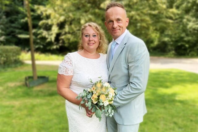 Stephanie und Marc Lobinger stehen aneinandergeschmiegt mit dem Brautstrauß in der Hand auf einer Wiese neben dem Hertener Rathaus.