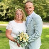 Stephanie und Marc Lobinger stehen aneinandergeschmiegt mit dem Brautstrauß in der Hand auf einer Wiese neben dem Hertener Rathaus.