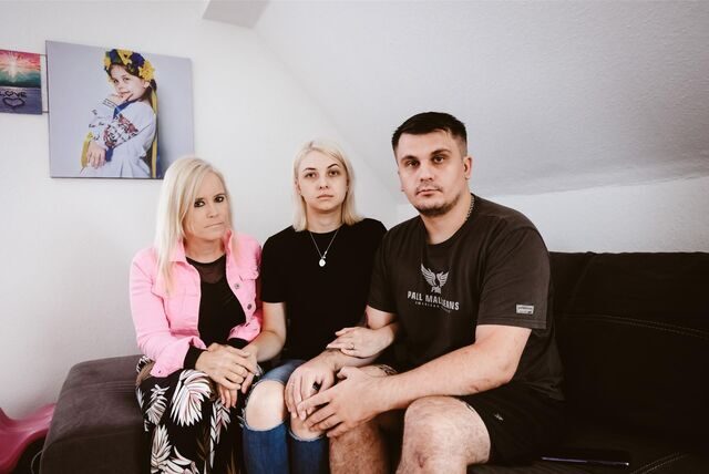 Eine Familie sitzt auf dem Sofa vor einem Foto ihrer verstorbenen kleinen Tochter.