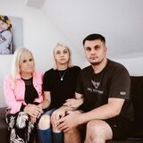 Eine Familie sitzt auf dem Sofa vor einem Foto ihrer verstorbenen kleinen Tochter.
