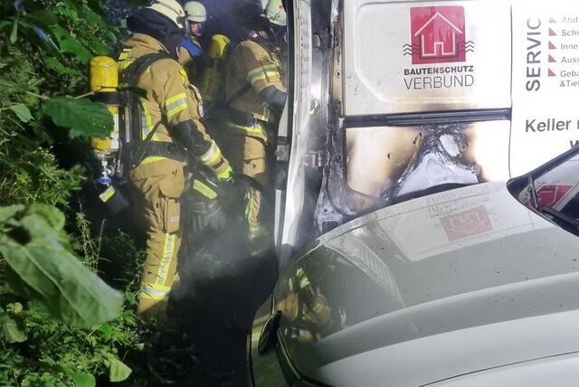 Feuerwehrleute stehen hinter einem Kleintransporter, den sie gerade gelöscht haben.