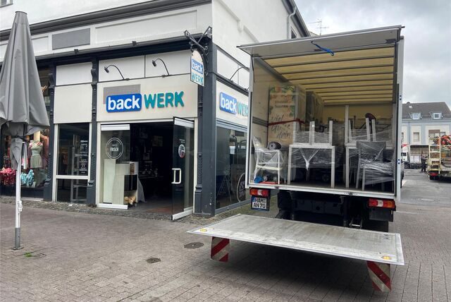 Ein Möbeltransporter steht neben einer Backwerk-Filiale