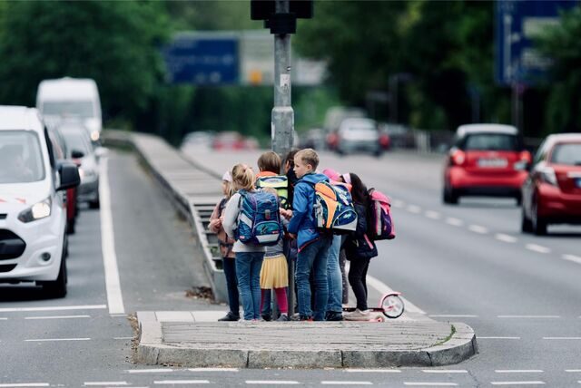 Eine Schülergruppe testet einen eventuellen, künftigen Schulweg und steht auf einer Verkehrsinsel inmitten der viel befahrenen Miquelallee.