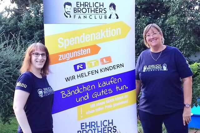 Zwei Frauen stehen vor einem Banner des Ehrlich Brothers Fanclub, das über den karitativen Einsatz aufklärt.