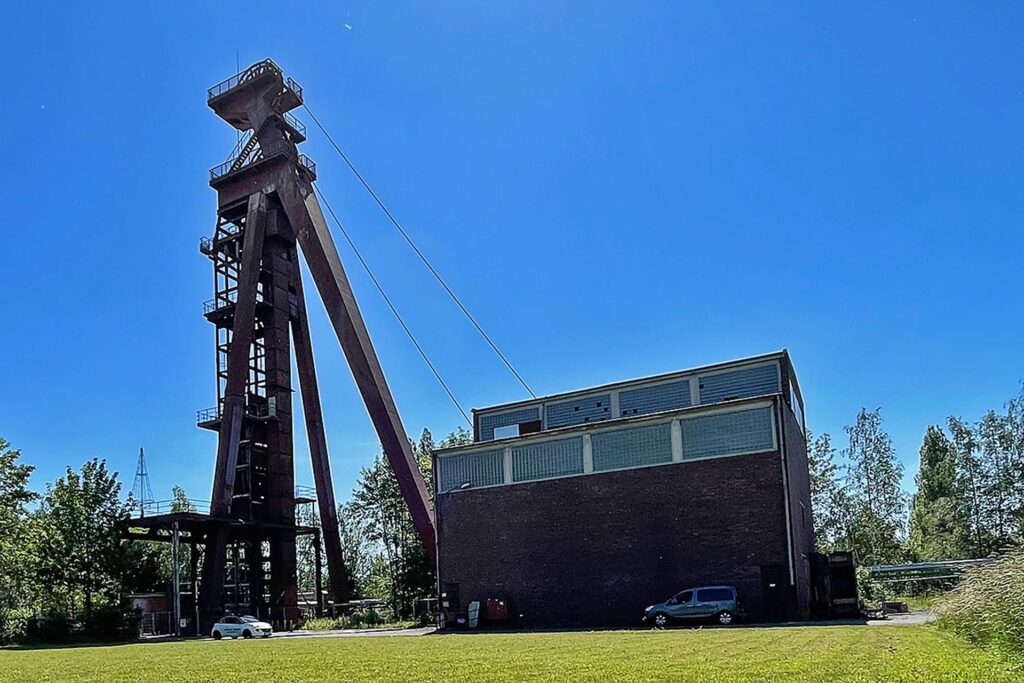 Gelände und Förderturm der Zeche Monopol in Kamen im Sommer. Davor eine grüne Wiese, im Hintergrund der blaue Himmel.