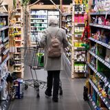 Eine Frau läuft mit ihrem Einkaufswagen durch einen Supermarkt.