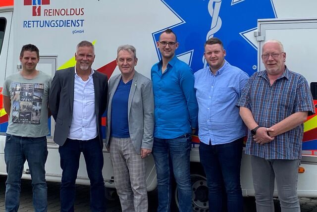 Belegschaftsmitglieder, Gewerkschaftsvertreter und Geschäftsführung stellen sich vor einem Rettungswagen für ein Gruppenbild auf. Anlass war die Vereinbarung eines Haustarifvertrages.