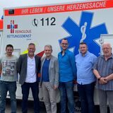 Belegschaftsmitglieder, Gewerkschaftsvertreter und Geschäftsführung stellen sich vor einem Rettungswagen für ein Gruppenbild auf. Anlass war die Vereinbarung eines Haustarifvertrages.