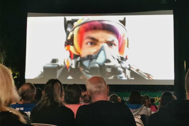 Eine Kinoleinwand, davor Publikum. Auf der Leinwand ein Moment des Films „Maverick“, während die Hauptfigur im Jet fliegt.