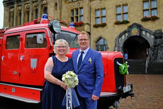 Brautpaar Reinhild Vadder und Uwe Starke stehen nach ihrer Trauung vor dem Rathaus in Recklinghausen, im Hintergrund steht ein historisches Löschfahrzeug der Feuerwehr, das mit Brautschmuck verziert ist