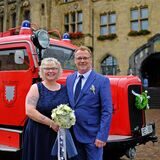 Brautpaar Reinhild Vadder und Uwe Starke stehen nach ihrer Trauung vor dem Rathaus in Recklinghausen, im Hintergrund steht ein historisches Löschfahrzeug der Feuerwehr, das mit Brautschmuck verziert ist