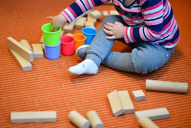 Ein Kind spielt auf einem Teppich mit Holzklötzchen und bunten Bechern.