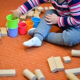 Ein Kind spielt auf einem Teppich mit Holzklötzchen und bunten Bechern.