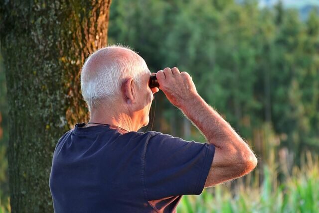 Ein älterer Mann blickt mit einem Fernglas in die Landschaft.