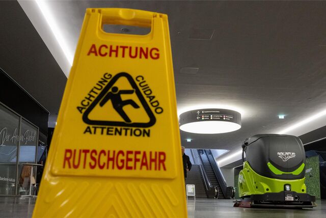 Ein Reinigungsroboter auf einer öffentlichen Fläche. Daneben ein Schild, das vor Rutschgefahr warnt.